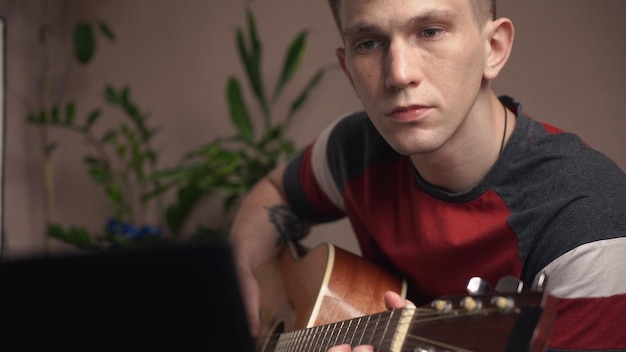 Young man learning to play acoustic guitar online at home closeup