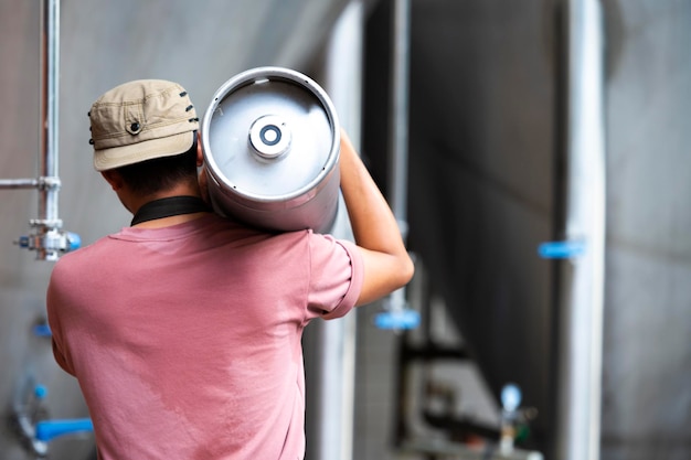 Young man in leather apron holding beer keg at modern brewery craft brewery worker