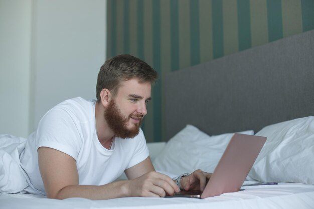 Young man lies and use laptop in bed in the morning concept online learning work shopping