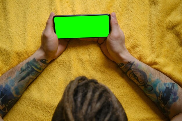 Young man lies on yellow blanket and uses phone to work or browse the Internet online watching movie