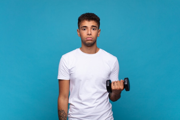 young man lifting a sumbbell feeling sad and whiney with an unhappy look, crying with a negative and frustrated attitude