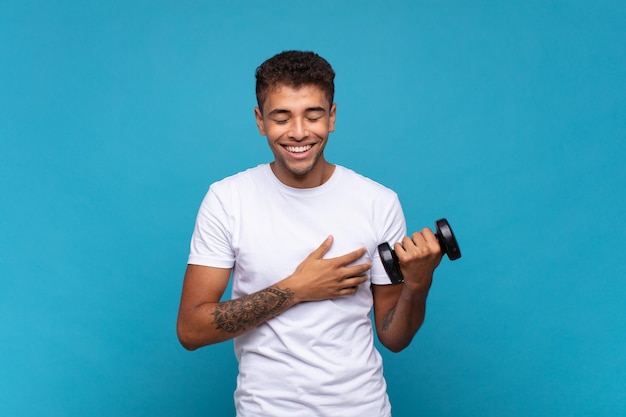 Photo young man lifting a sumbbell laughing out loud at some hilarious joke, feeling happy and cheerful, having fun