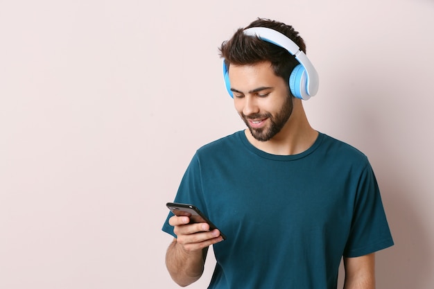 Young man listening to audiobook on light background