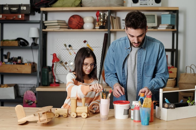 Young man and little girl in casualwear preparing paints and paintbrushes
