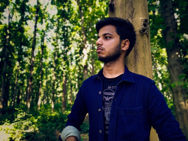 Young man looking away while standing in forest