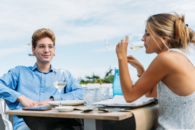 ビーチフロントのレストランのテーブルに座ってワインを飲む金髪の熟女を見て若い男