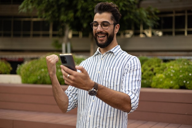 Young man looking at cell phone celebrating in the street