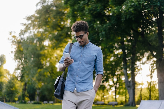 Молодой человек смотрит на мобильный телефон в парке