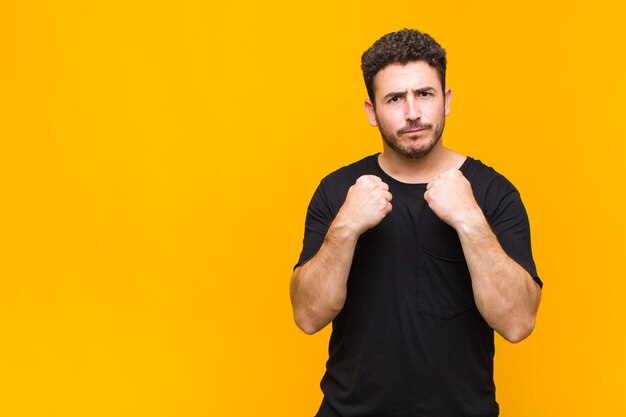 Young man looking confident, angry, strong and aggressive, with fists ready to fight in boxing position