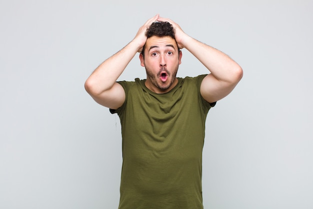 Young man looking excited and surprised, open-mouthed with both hands on head, feeling like a lucky winner