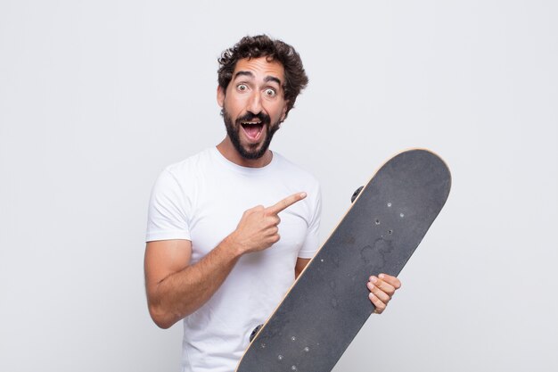 Young man looking excited and surprised pointing to the side and upwards to copy space