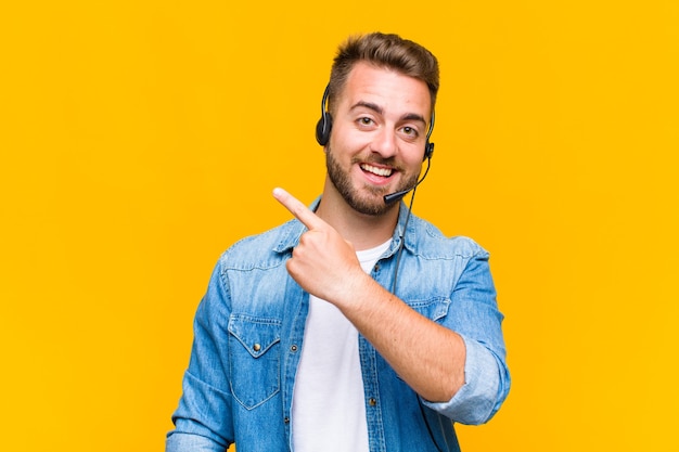 Young man looking excited and surprised pointing to the side and upwards to copy space