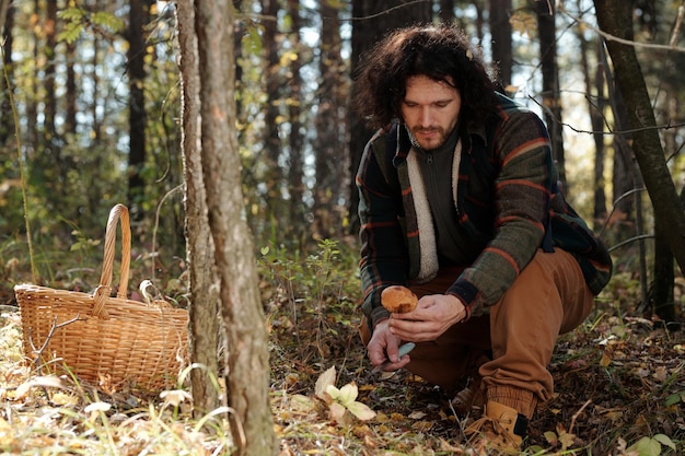 Young man looking at fresh boletus mushroom in his hand