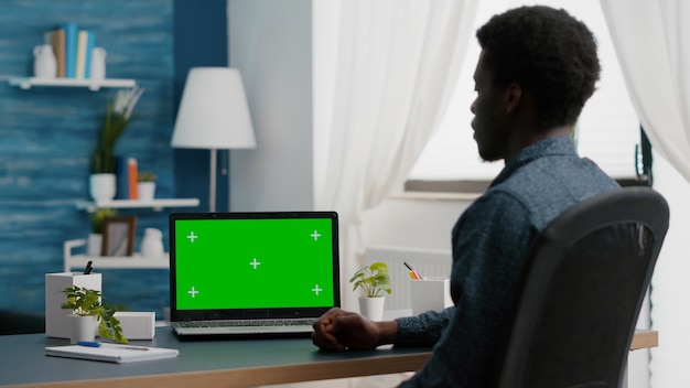 молодой человек смотрит на зеленый экран, изолированный макет дисплея ноутбука в яркой квартире