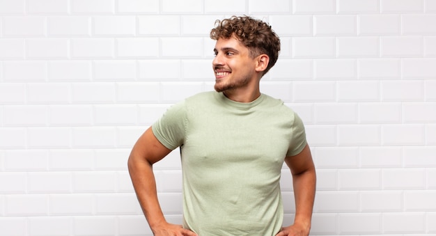 Young man looking happy, cheerful and confident, smiling proudly and looking to side with both hands on hips