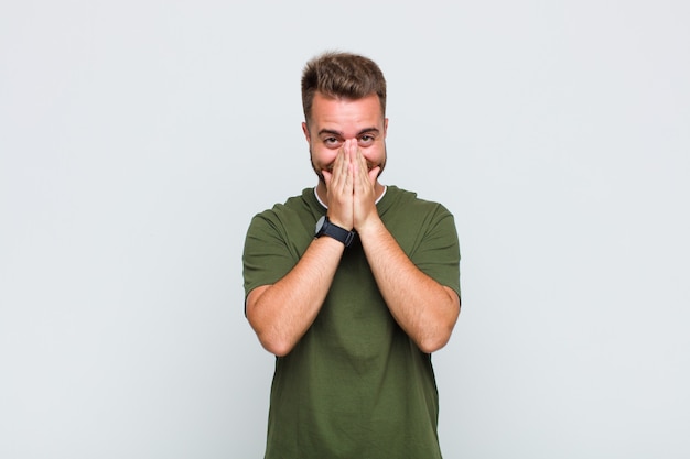 Young man looking happy, cheerful, lucky and surprised covering mouth with both hands