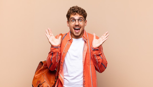 Young man looking happy and excited, shocked with an unexpected surprise with both hands open next to face. student concept