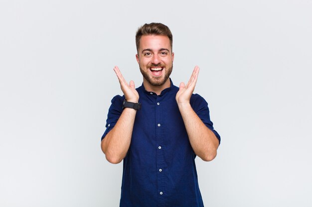 Young man looking happy and excited, shocked with an unexpected surprise with both hands open next to face