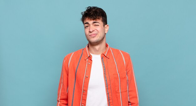 Young man looking happy and friendly, smiling and winking an eye at you with a positive attitude