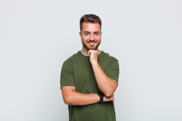 Young man looking happy and smiling with hand on chin, wondering or asking a question, comparing options