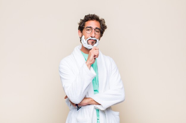 Young man looking happy and smiling with hand on chin, wondering or asking a question, comparing options