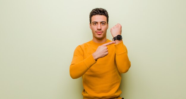 Young man looking impatient and angry, pointing at watch, asking for punctuality, wants to be on time over wall