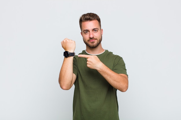 Young man looking impatient and angry, pointing at watch, asking for punctuality, wants to be on time