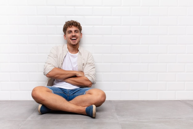 Photo young man looking like a happy, proud and satisfied achiever smiling with arms crossed