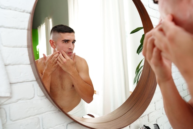 Young man looking in the mirror in the bathroom preparing for the day