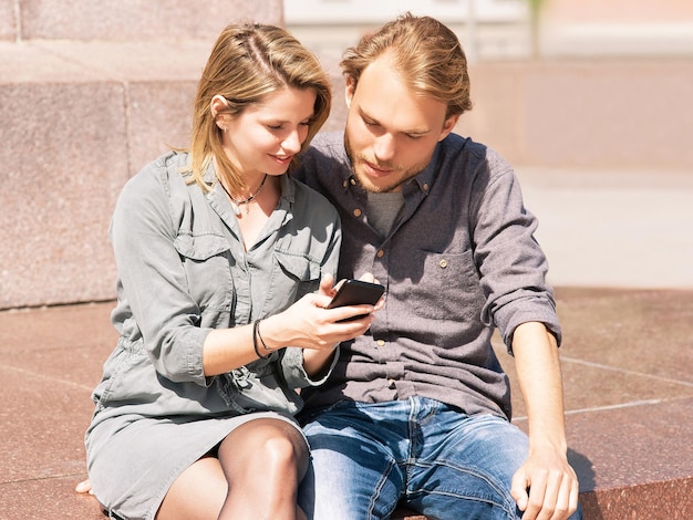 Young man looking at mobile phone of his girlfriend with interest and surprise as friendship and togetherness concept
