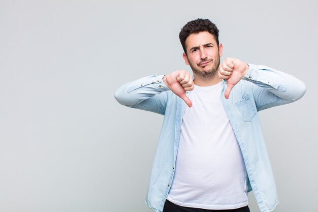 Young man looking sad, disappointed or angry, showing thumbs down in disagreement, feeling frustrated