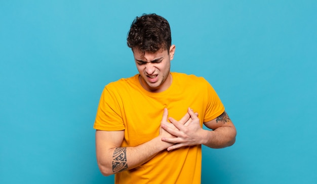 Young man looking sad, hurt and heartbroken, holding both hands close to heart, crying and feeling depressed