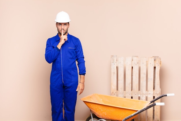 Young man looking serious and cross with finger pressed to lips demanding silence or quiet, keeping a secret construction concept