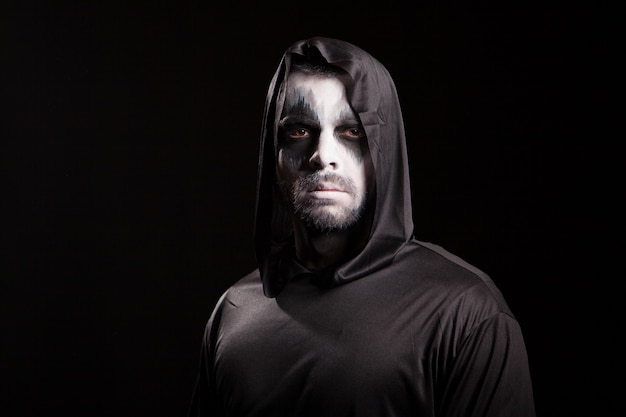 Young man looking serious into the camera dressed up like grim reaper. Halloween costume.