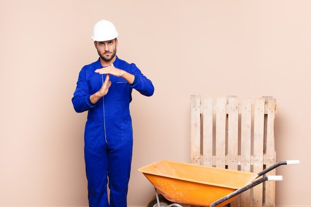 Young man looking serious, stern, angry and displeased, making time out sign construction concept