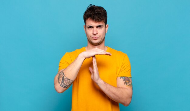 Young man looking serious, stern, angry and displeased, making time out sign