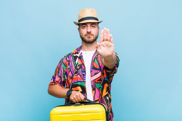 Young man looking serious, stern, displeased and angry showing open palm making stop gesture