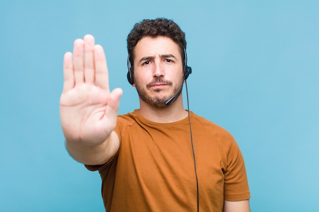 Young man looking serious, stern, displeased and angry showing open palm making stop gesture