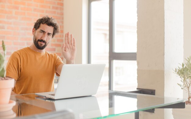 Young man looking serious stern displeased and angry showing open palm making stop gesture