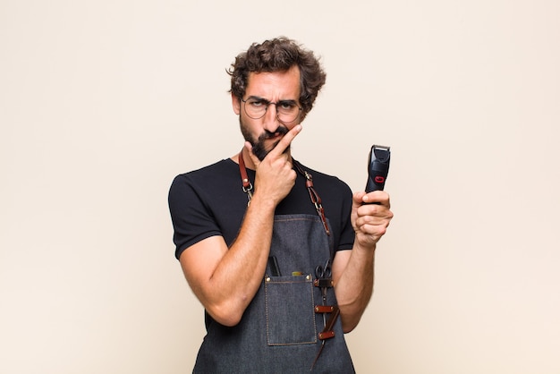 Young man looking serious, thoughtful and distrustful, with one arm crossed and hand on chin, weighting options