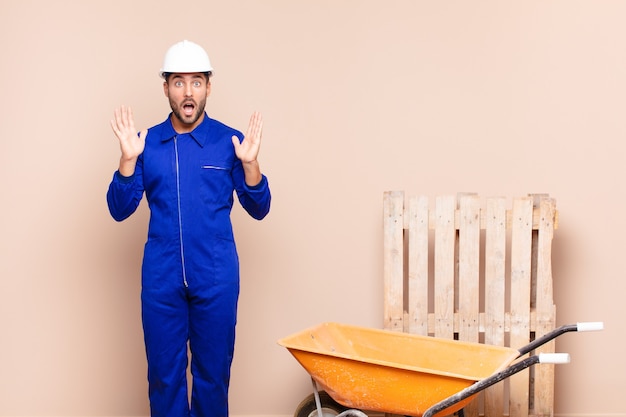 Young man looking shocked and astonished, with jaw dropped in surprise when realizing something unbelievable construction concept