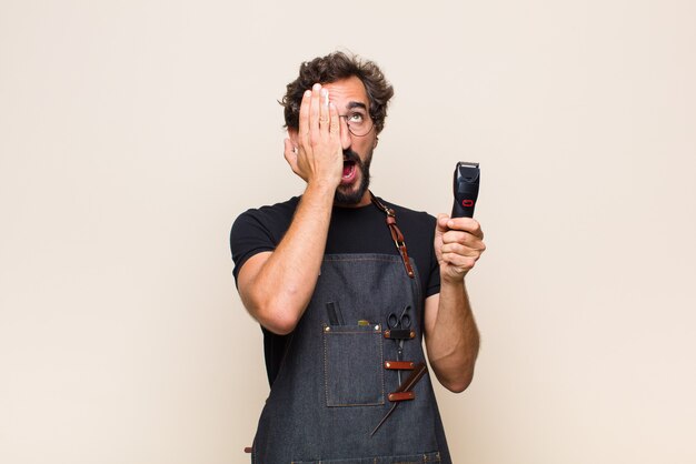 Young man looking sleepy, bored and yawning, with a headache and one hand covering half the face