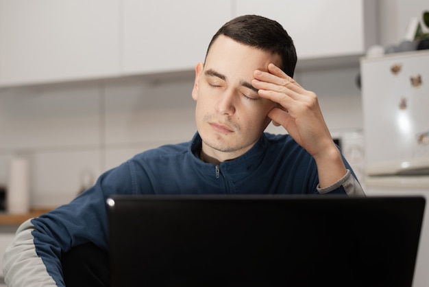 A young man looking stressed while using a laptop to work from home