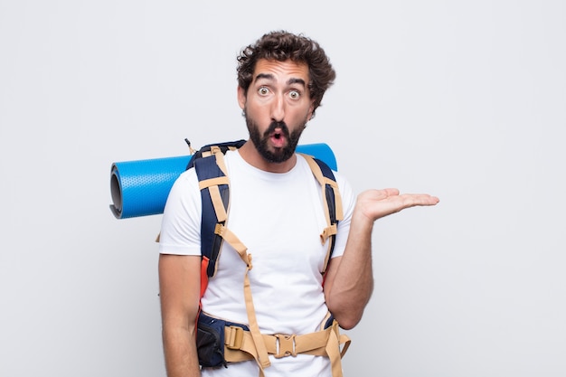 Young man looking surprised and shocked, with jaw dropped holding an object with an open hand on the side