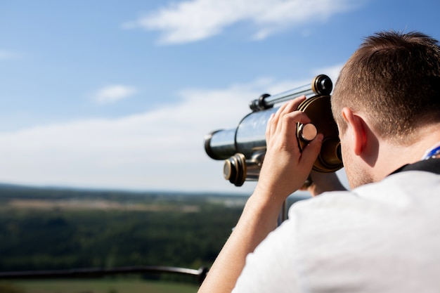 Photo young man looking through binoculars to the landscape panorama. space for text