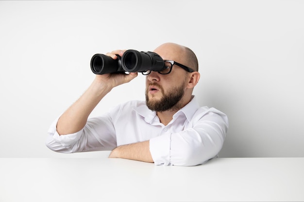 Foto giovane che guarda attraverso il binocolo che dà una occhiata al tavolo su uno sfondo bianco