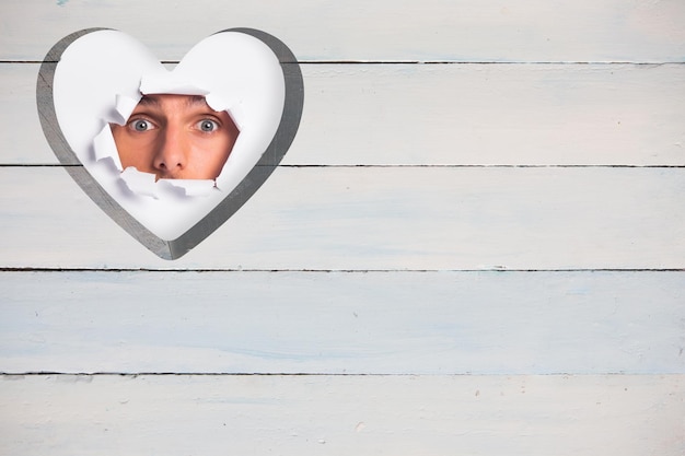 Young man looking through paper rip against heart in wood