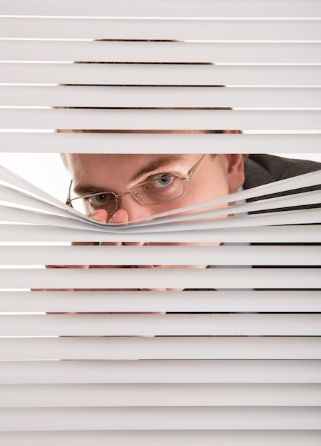 Photo a young man looking through window blinds