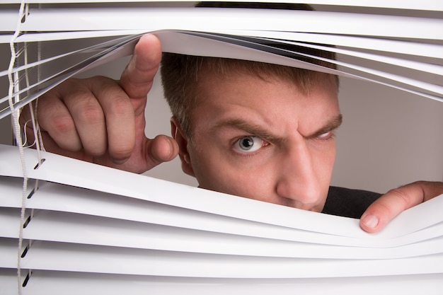 Photo a young man looking through window blinds