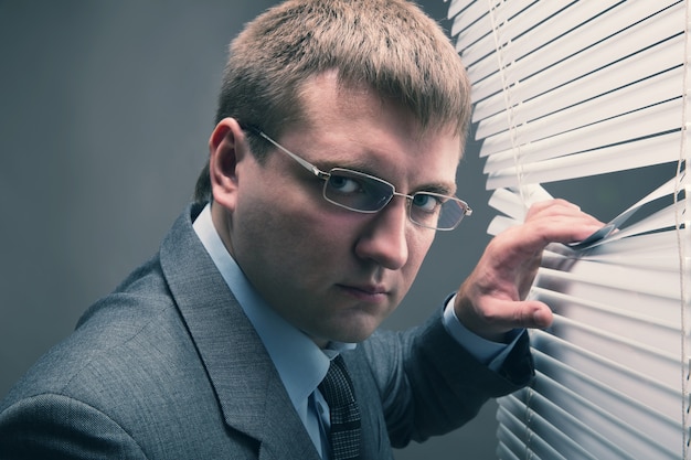 A young man looking through window blinds